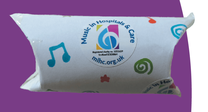 A toilet roll tube that has been made into a percussion instrument and decorated with music notes and a Music in Hospitals & Care logo sticker.