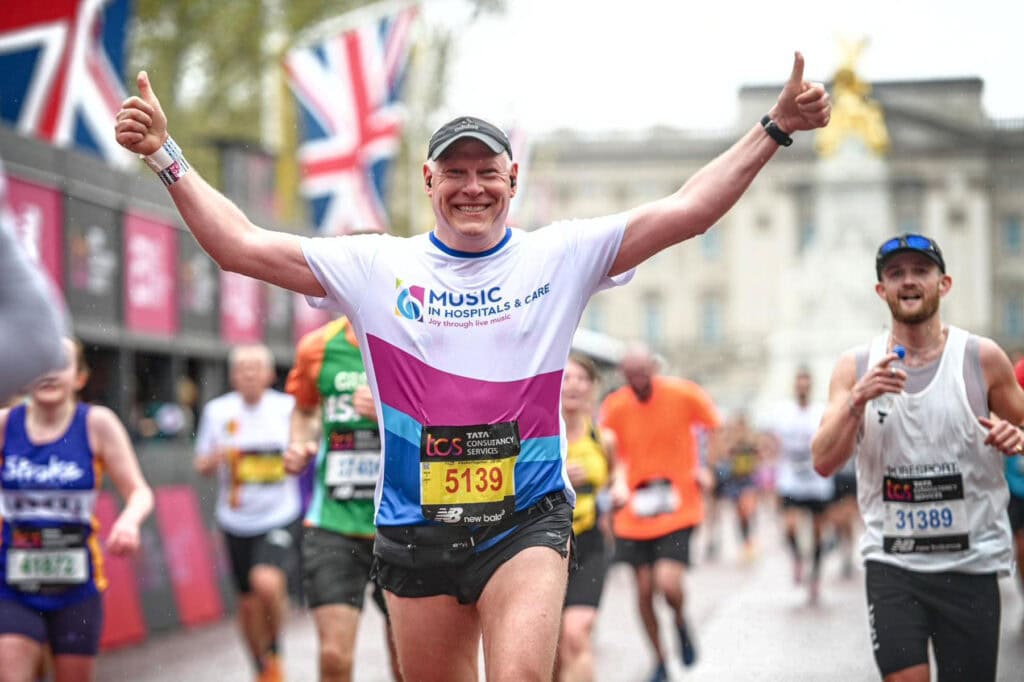 London Marathon runner in a Music in Hospitals & Care top runs with his thumbs up.