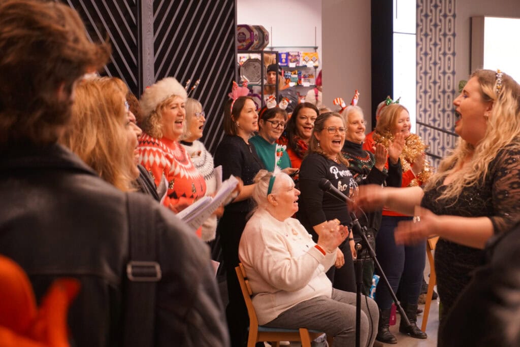 A choir in Christmas headwear and outfits led by a conductor sing in John Lewis.