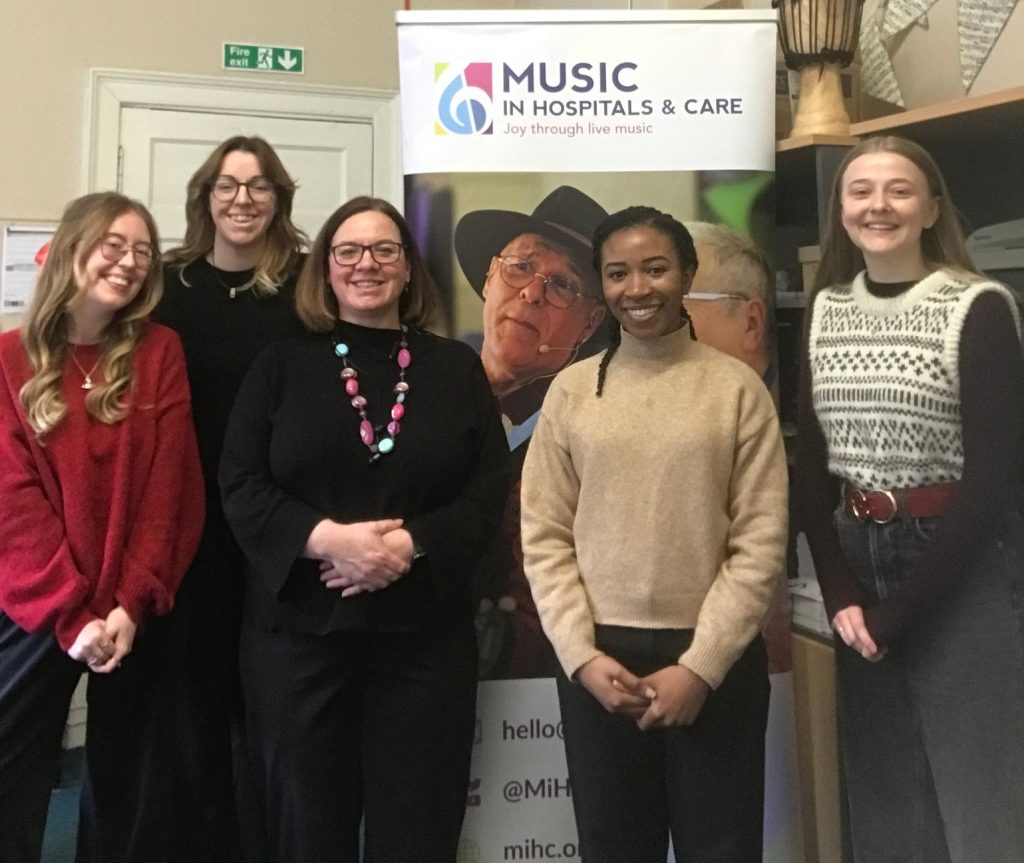 Music in Hospitals & Care Student placement team standing together and smiling in front of a charity banner