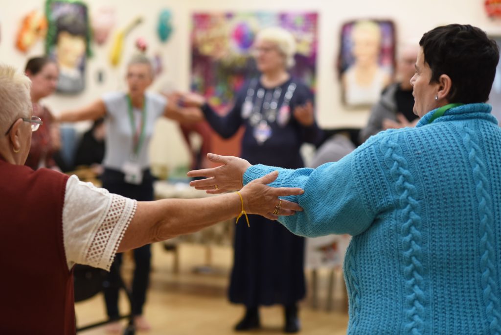 Musician performing live in a ward, seated with a guitar and engaging patients during a Music in Hospitals & Care session
