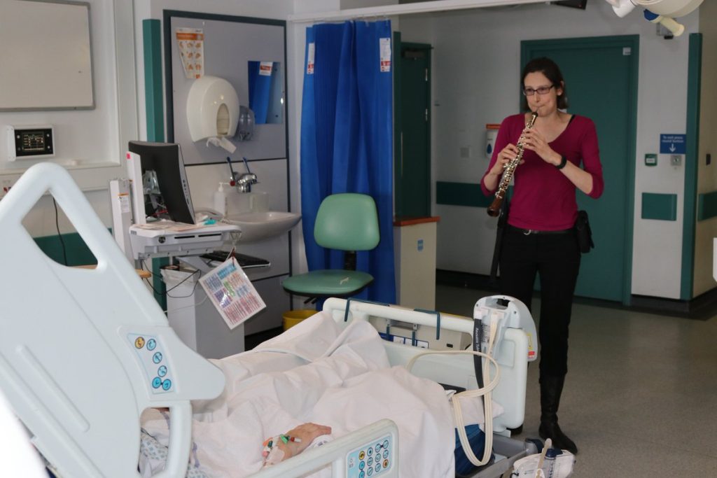 Musician playing oboe at a patient’s bedside in hospital during a Music in Hospitals & Care session.