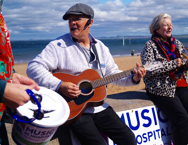 Musician playing guitar and singing at a seaside fundraising event for Music in Hospitals & Care.