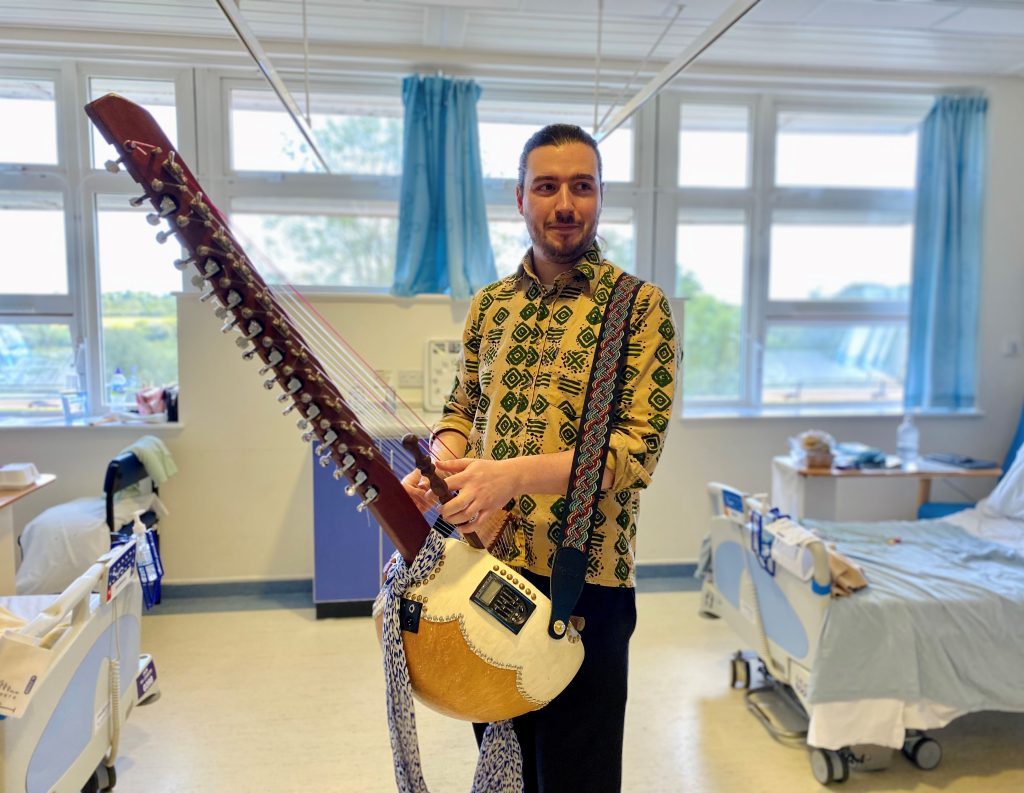 Musician standing in a hospital ward holding a kora before performing for patients during a Music in Hospitals & Care session.