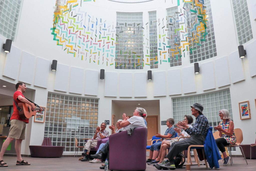 Musician playing guitar to group of people at Redwoods centre