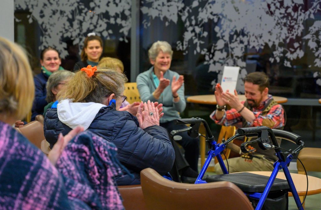 Audience members clapping and smiling during a community live music session organised by Music in Hospitals & Care.