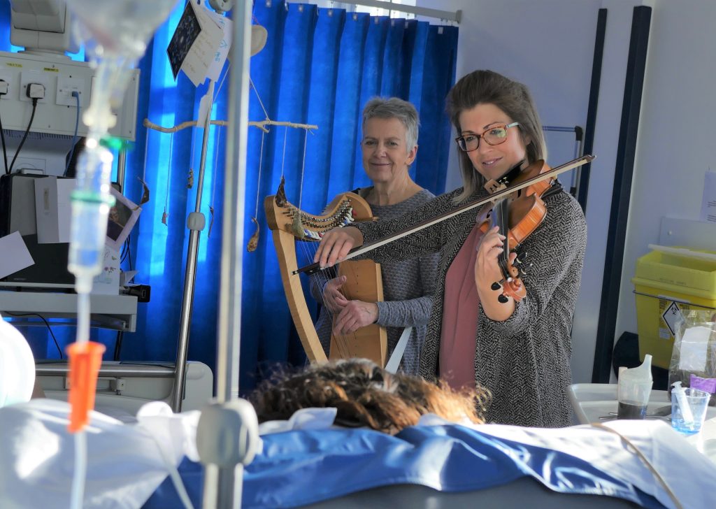 Violinist and harpist performing live at a hospital bedside for a patient as part of a Music in Hospitals & Care session.