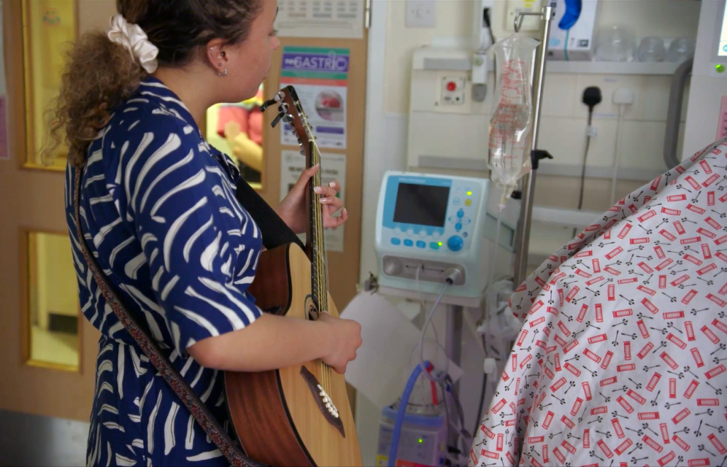 Woman playing guitar to patient in hospital